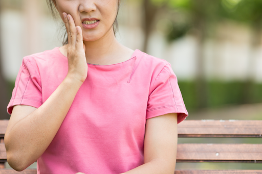 A woman on a park bench holding the side of her mouth with one hand.