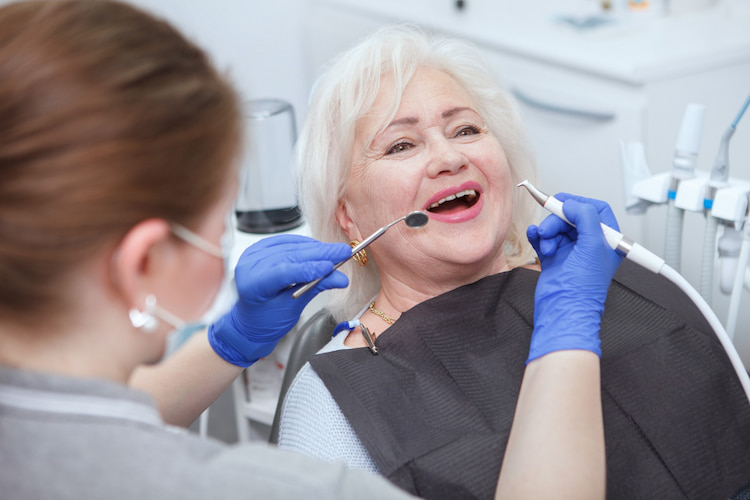 a senior patient has opened her mouth, so a dentist can perform a dental treatment.